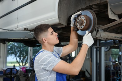 Photo of Young auto mechanic fixing lifted car at automobile repair shop