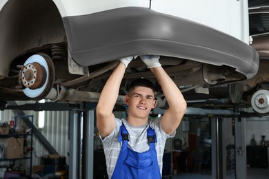 Photo of Young auto mechanic fixing lifted car at automobile repair shop