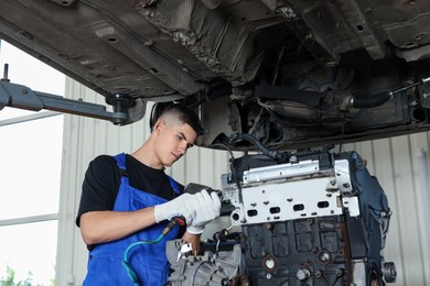 Young auto mechanic fixing motor at automobile repair shop, low angle view. Car diagnostic