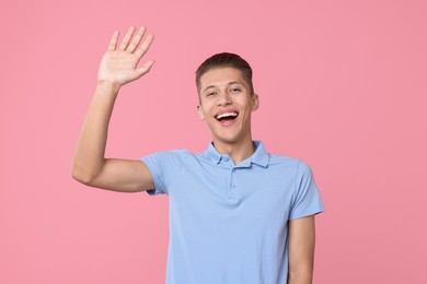 Photo of Goodbye gesture. Happy young man waving on pink background