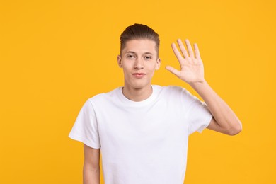 Photo of Goodbye gesture. Happy young man waving on orange background