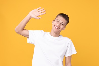 Photo of Goodbye gesture. Happy young man waving on orange background