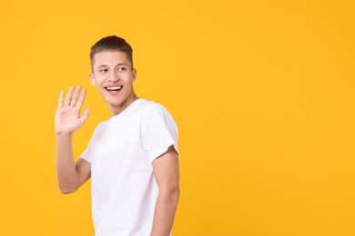Photo of Goodbye gesture. Happy young man waving on orange background, space for text