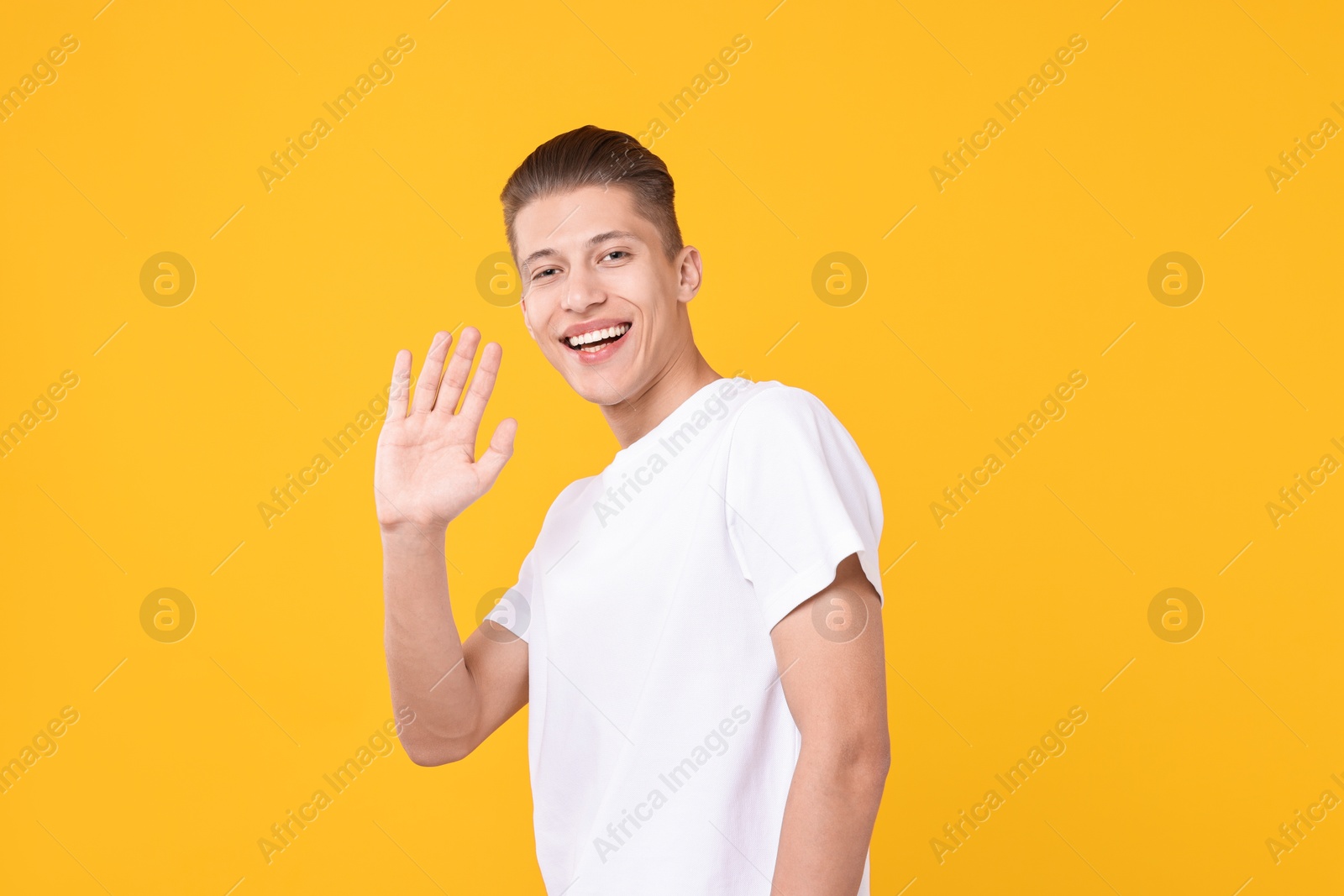 Photo of Goodbye gesture. Happy young man waving on orange background