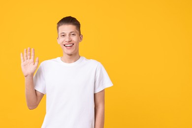 Photo of Goodbye gesture. Happy young man waving on orange background, space for text