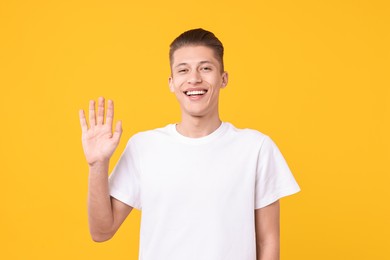 Photo of Goodbye gesture. Happy young man waving on orange background