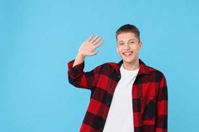 Goodbye gesture. Happy young man waving on light blue background, space for text