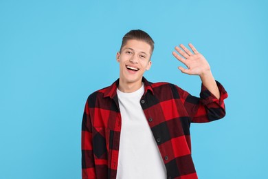 Goodbye gesture. Happy young man waving on light blue background