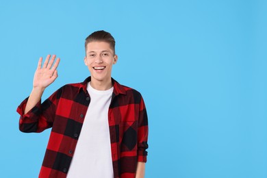 Goodbye gesture. Happy young man waving on light blue background, space for text