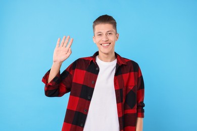 Photo of Goodbye gesture. Happy young man waving on light blue background