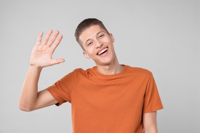 Photo of Goodbye gesture. Happy young man waving on light grey background