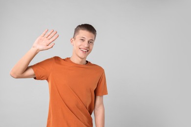 Photo of Goodbye gesture. Happy young man waving on light grey background, space for text