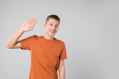 Goodbye gesture. Happy young man waving on light grey background, space for text