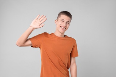 Goodbye gesture. Happy young man waving on light grey background