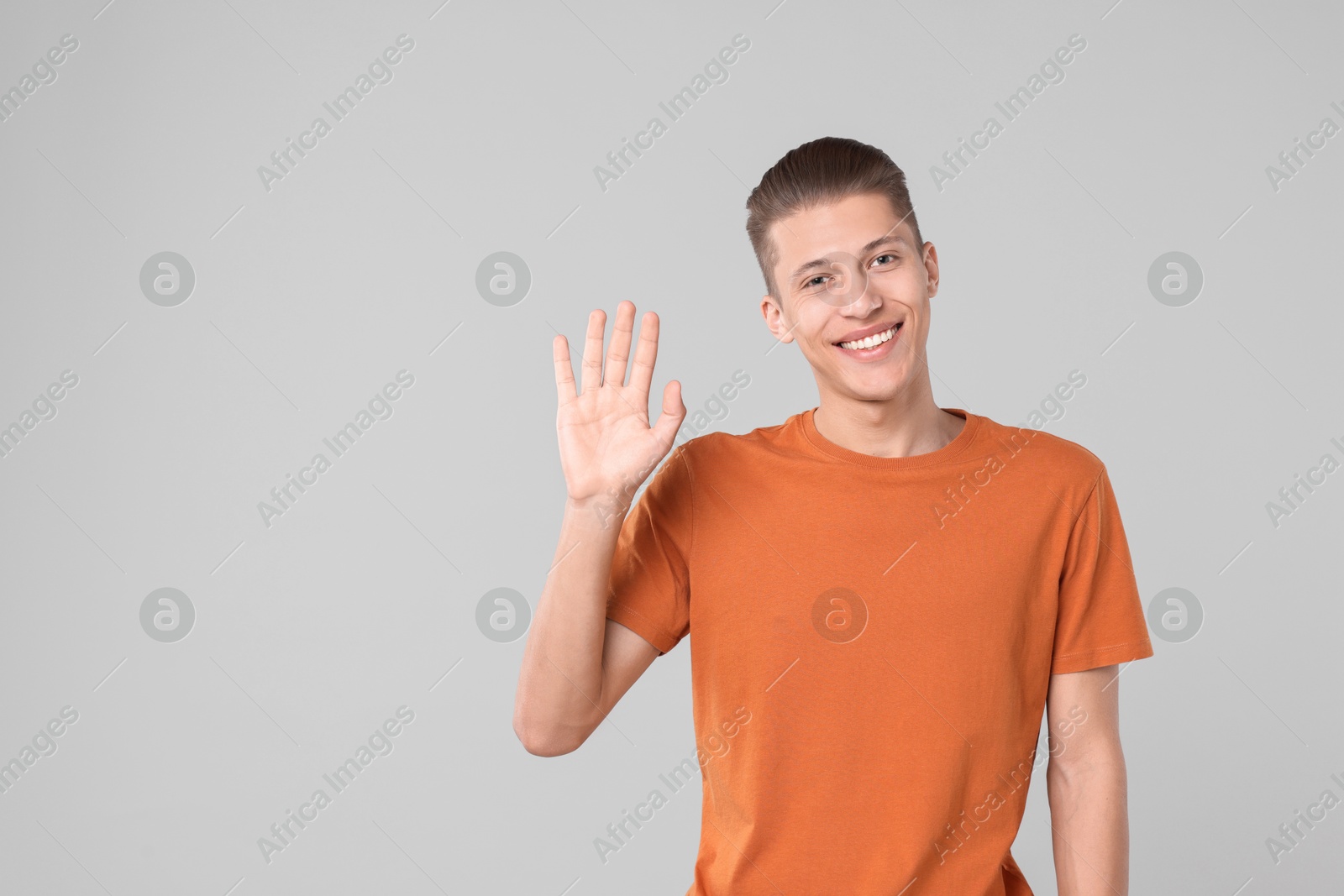 Photo of Goodbye gesture. Happy young man waving on light grey background, space for text