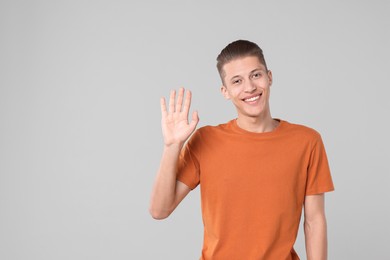 Goodbye gesture. Happy young man waving on light grey background, space for text