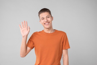 Goodbye gesture. Happy young man waving on light grey background