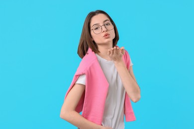 Beautiful teenage girl blowing kiss on light blue background