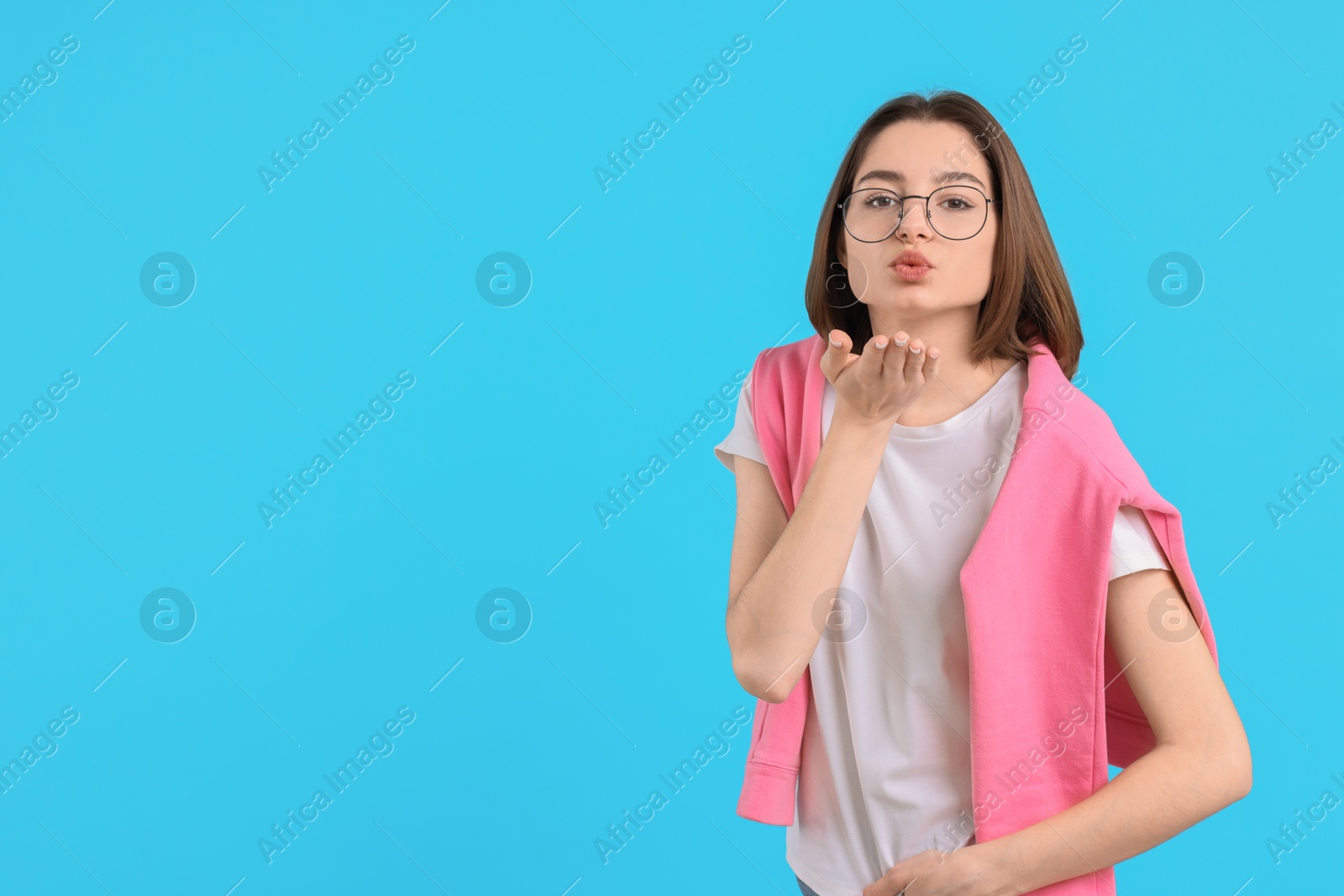 Photo of Beautiful teenage girl blowing kiss on light blue background, space for text