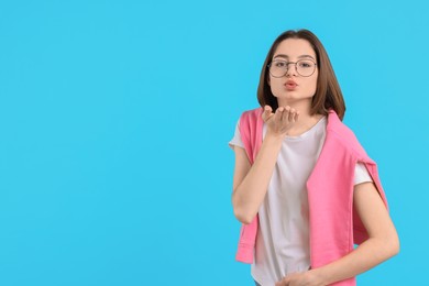 Beautiful teenage girl blowing kiss on light blue background, space for text