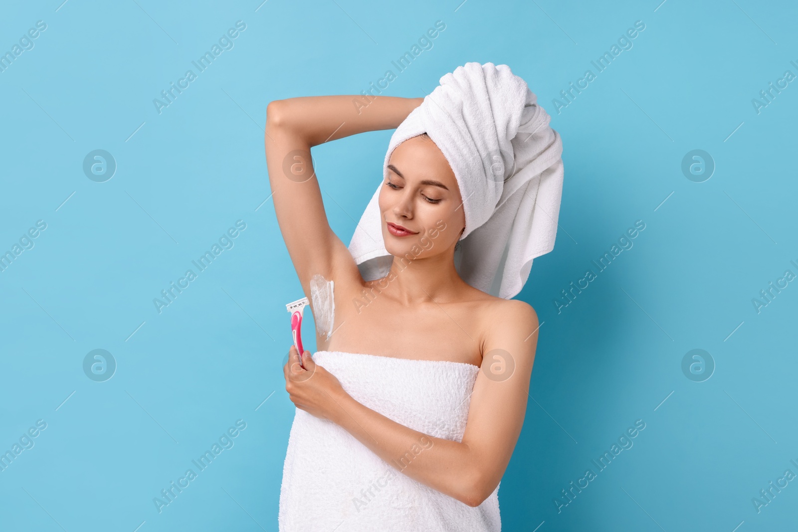 Photo of Beautiful woman shaving armpit on light blue background