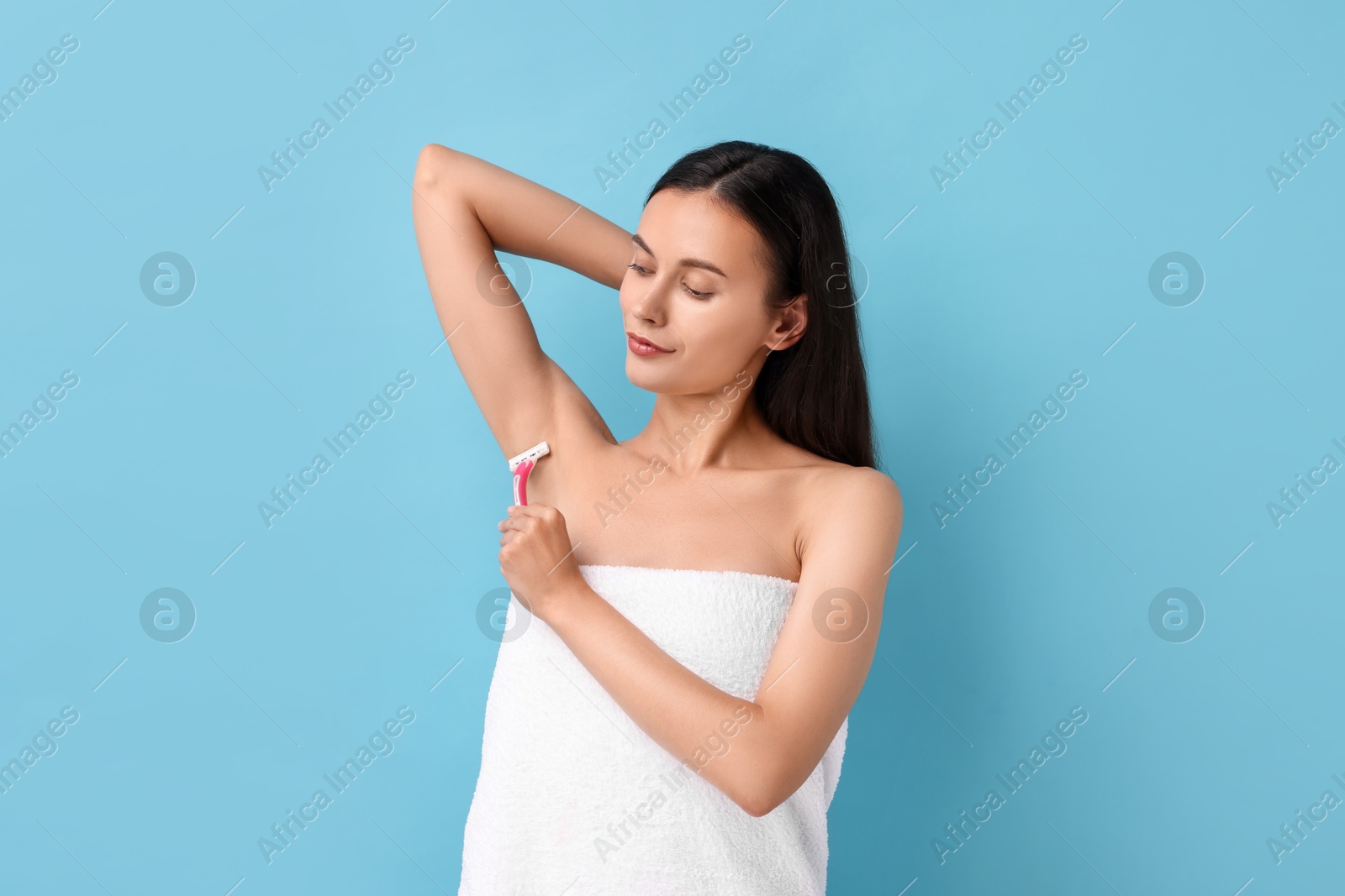 Photo of Beautiful woman shaving armpit on light blue background