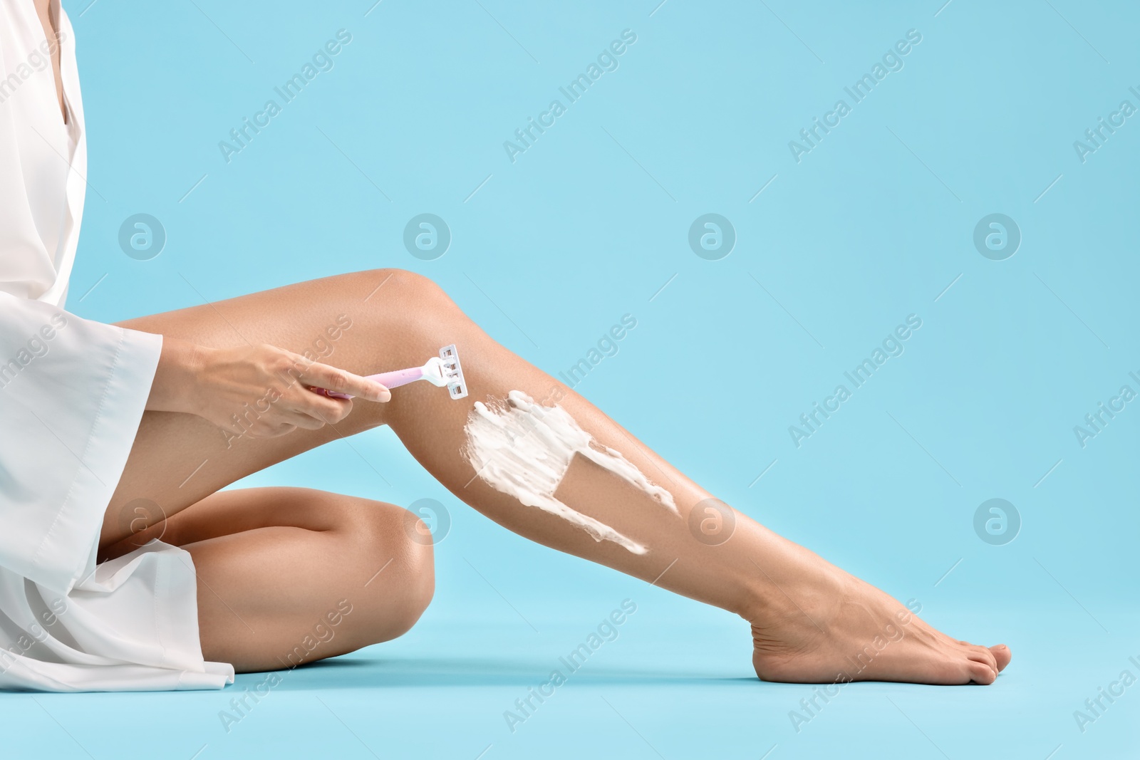 Photo of Woman shaving leg on light blue background, closeup. Space for text