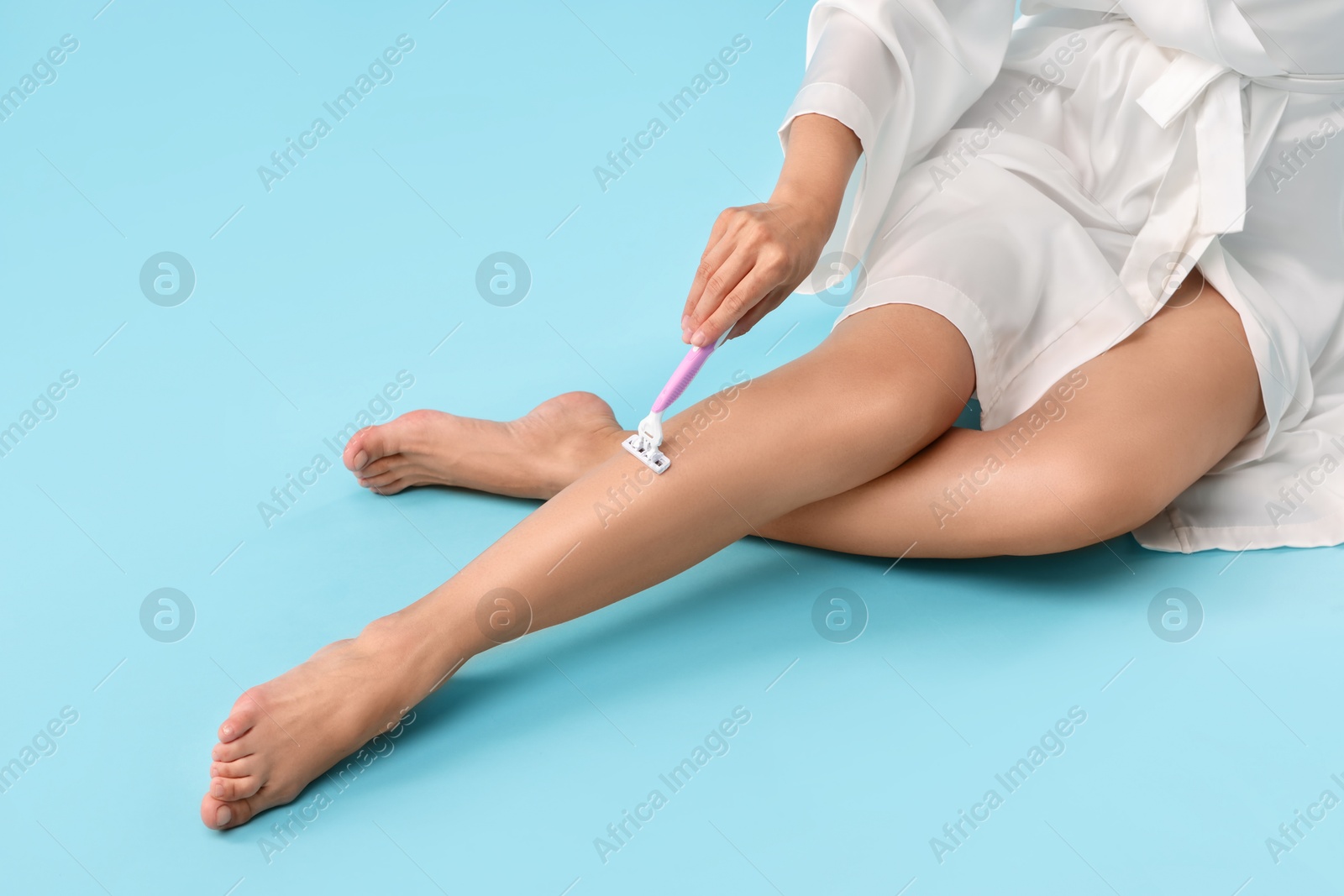 Photo of Woman shaving leg on light blue background, closeup