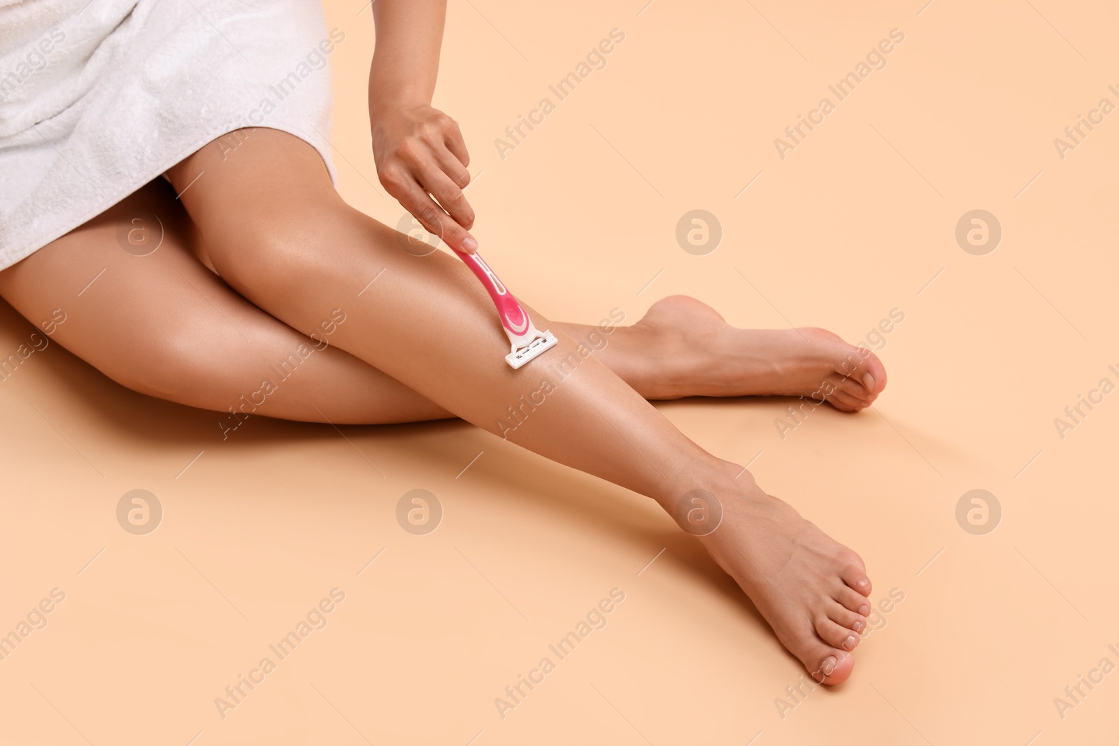 Photo of Woman shaving leg on beige background, closeup