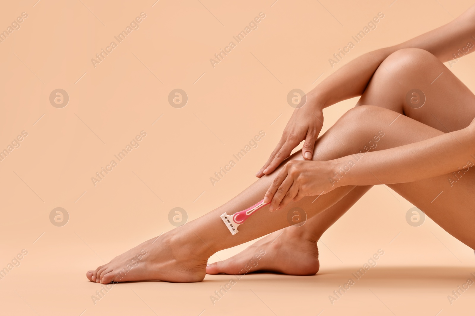 Photo of Woman shaving leg on beige background, closeup. Space for text