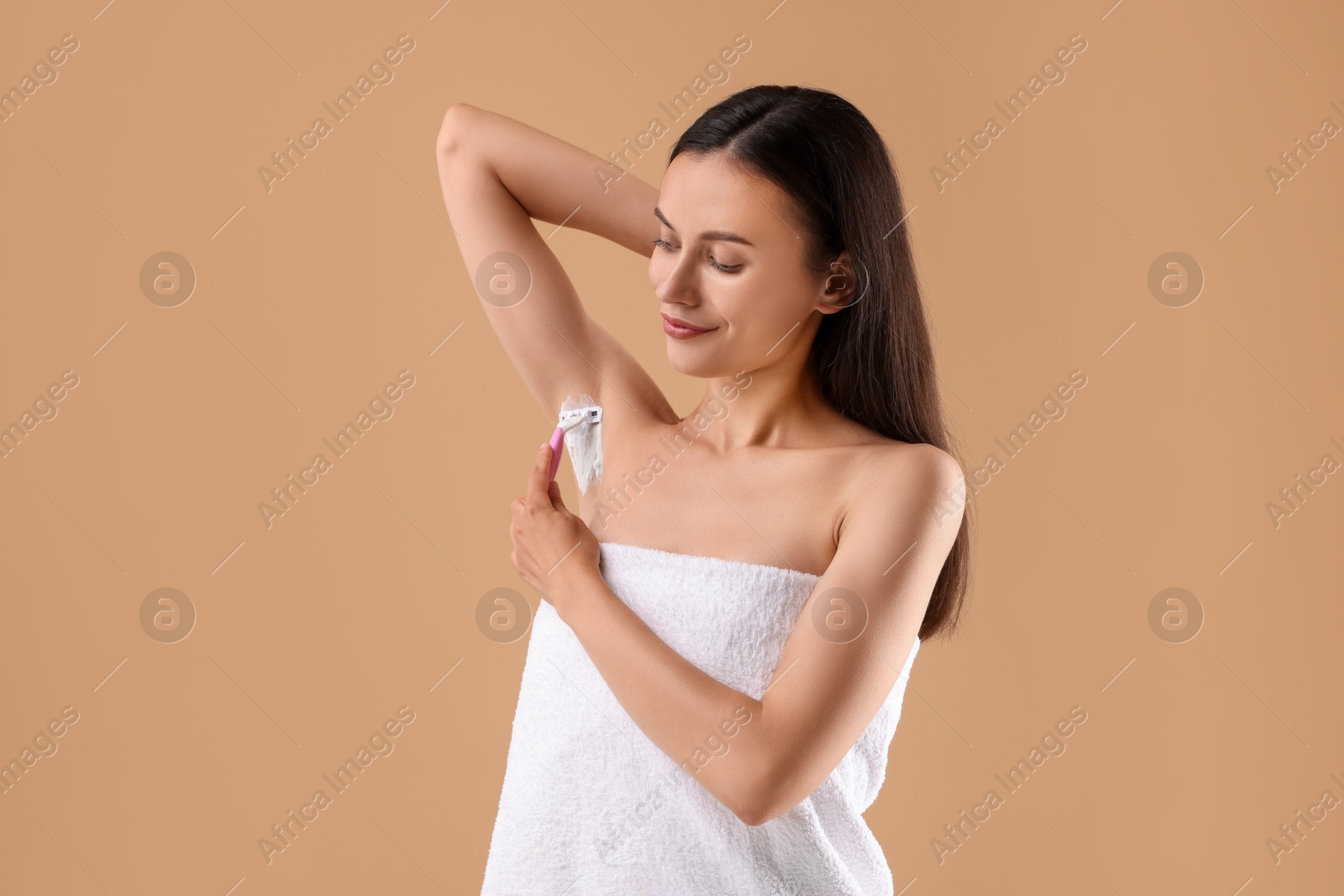 Photo of Beautiful woman shaving armpit on beige background