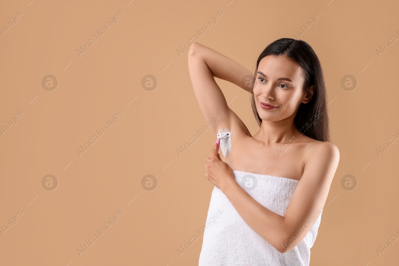 Photo of Beautiful woman shaving armpit on beige background. Space for text