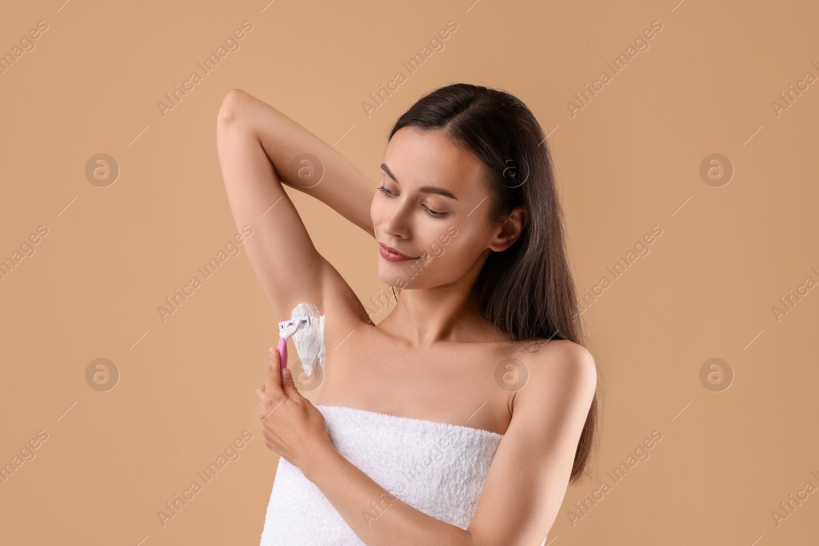 Photo of Beautiful woman shaving armpit on beige background