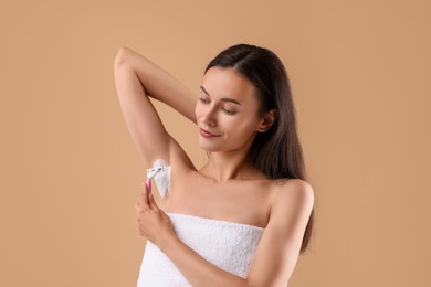 Photo of Beautiful woman shaving armpit on beige background