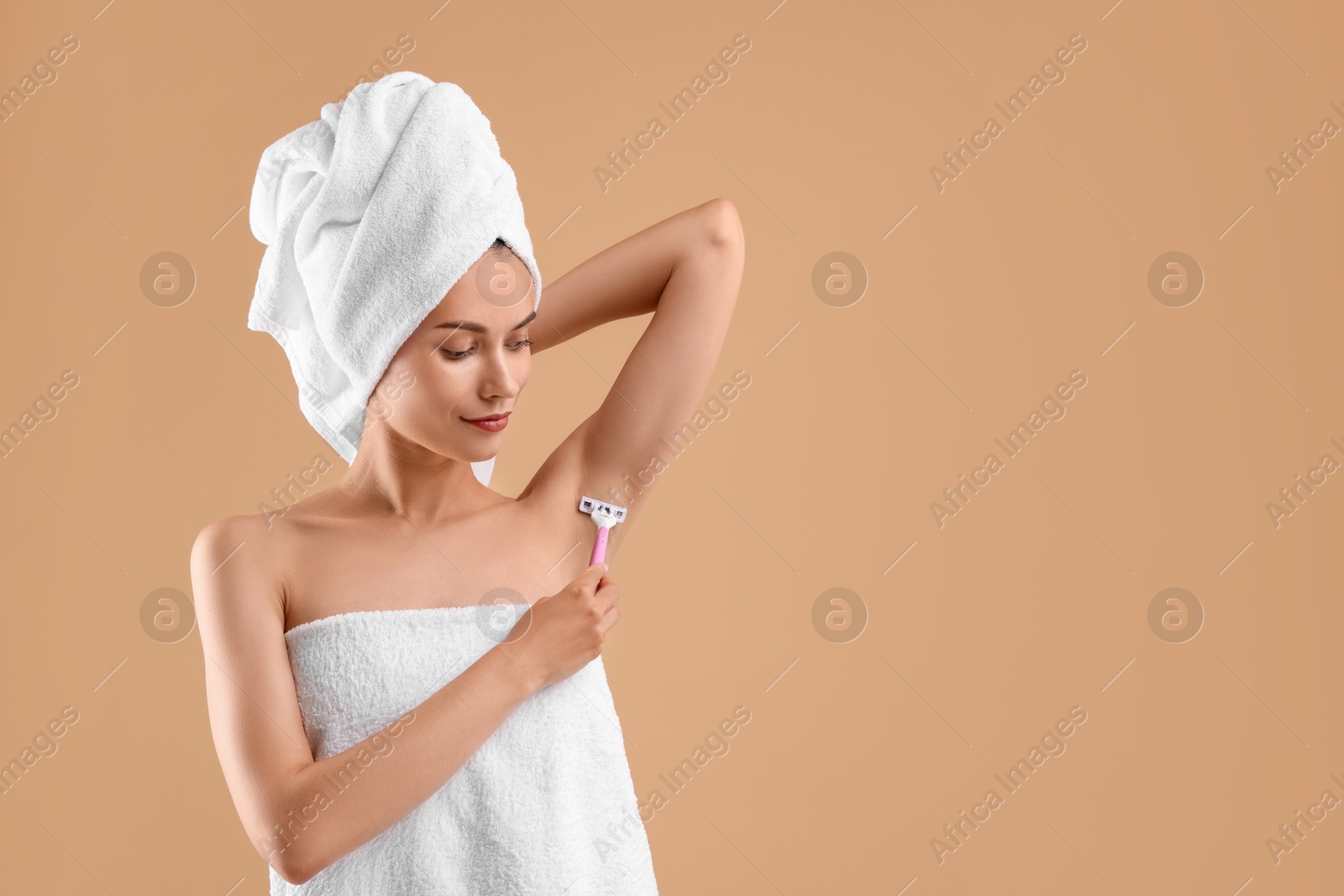 Photo of Beautiful woman shaving armpit on beige background. Space for text