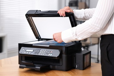 Woman using modern printer at workplace indoors, closeup