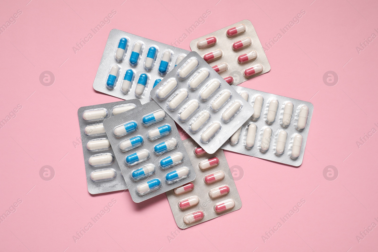 Photo of Antibiotic pills in blisters on pink background, top view