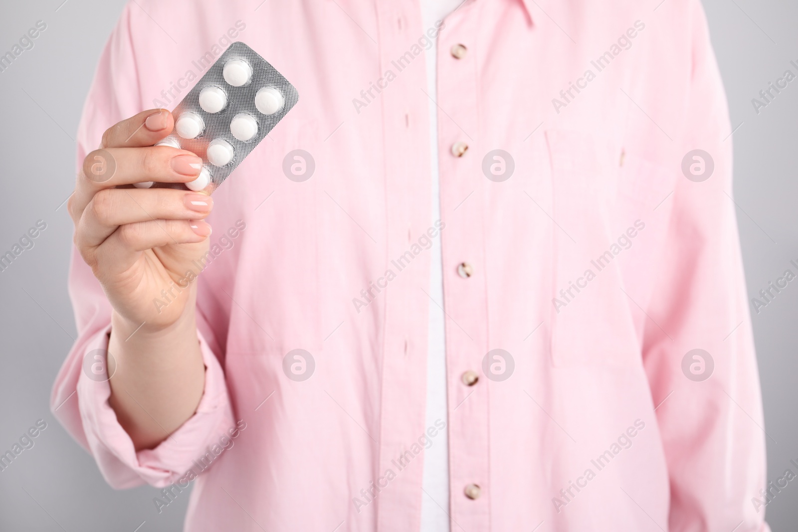 Photo of Woman holding blister with antibiotic pills on light grey background, closeup