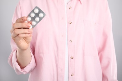 Woman holding blister with antibiotic pills on light grey background, closeup