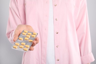 Photo of Woman holding blister with antibiotic pills on light grey background, closeup