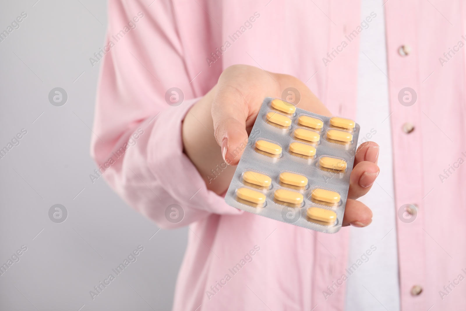 Photo of Woman holding blister with antibiotic pills on light grey background, closeup