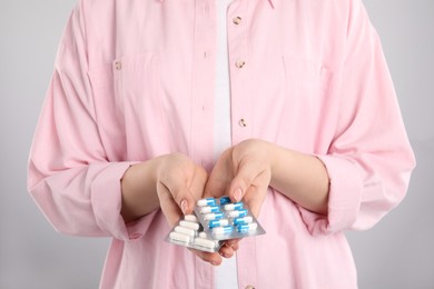 Photo of Woman holding blisters with antibiotic pills on light grey background, closeup