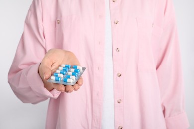 Photo of Woman holding blister with antibiotic pills on light background, closeup