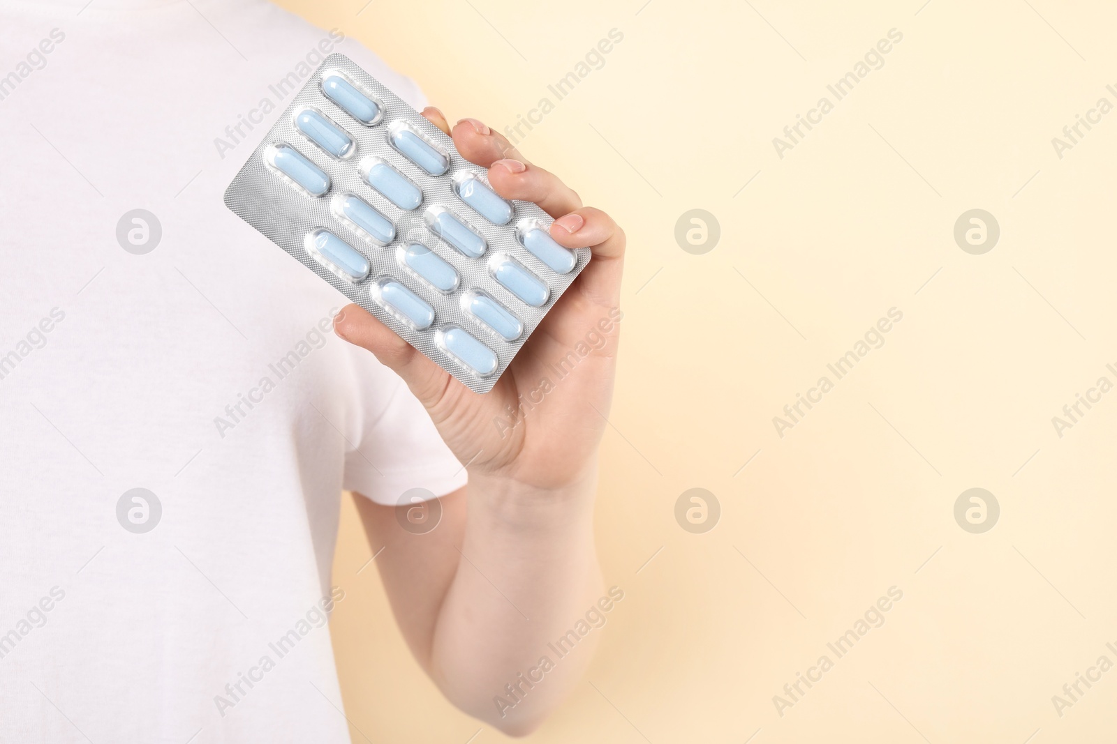 Photo of Woman holding blister with antibiotic pills on beige background, closeup. Space for text