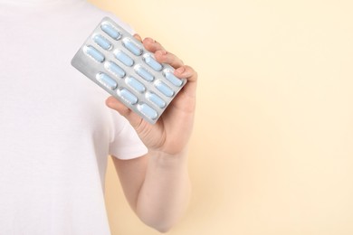 Photo of Woman holding blister with antibiotic pills on beige background, closeup. Space for text