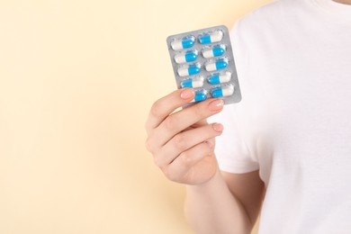 Woman holding blister with antibiotic pills on beige background, closeup. Space for text