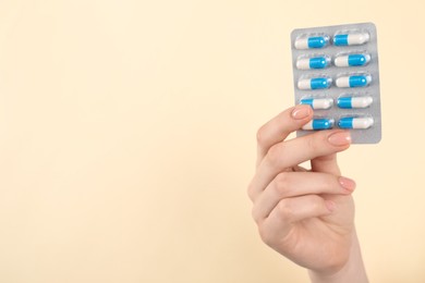 Woman holding blister with antibiotic pills on beige background, closeup. Space for text