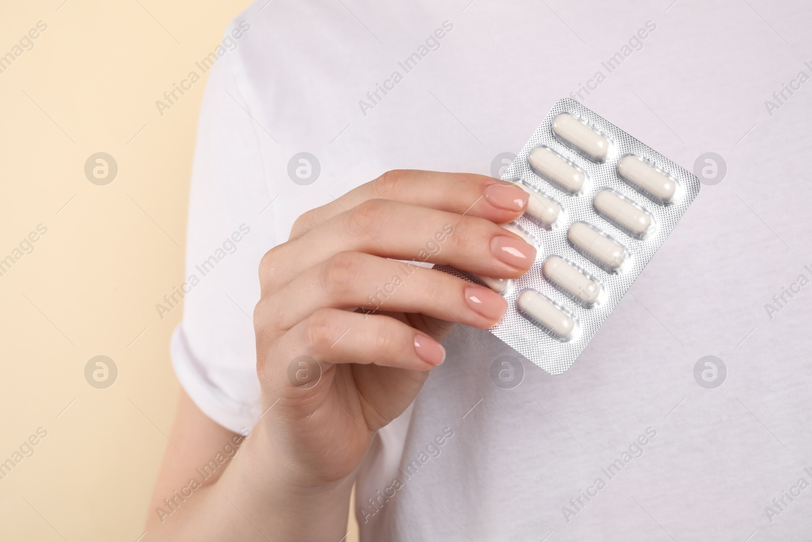 Photo of Woman holding blister with antibiotic pills on beige background, closeup