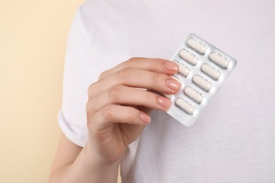 Photo of Woman holding blister with antibiotic pills on beige background, closeup