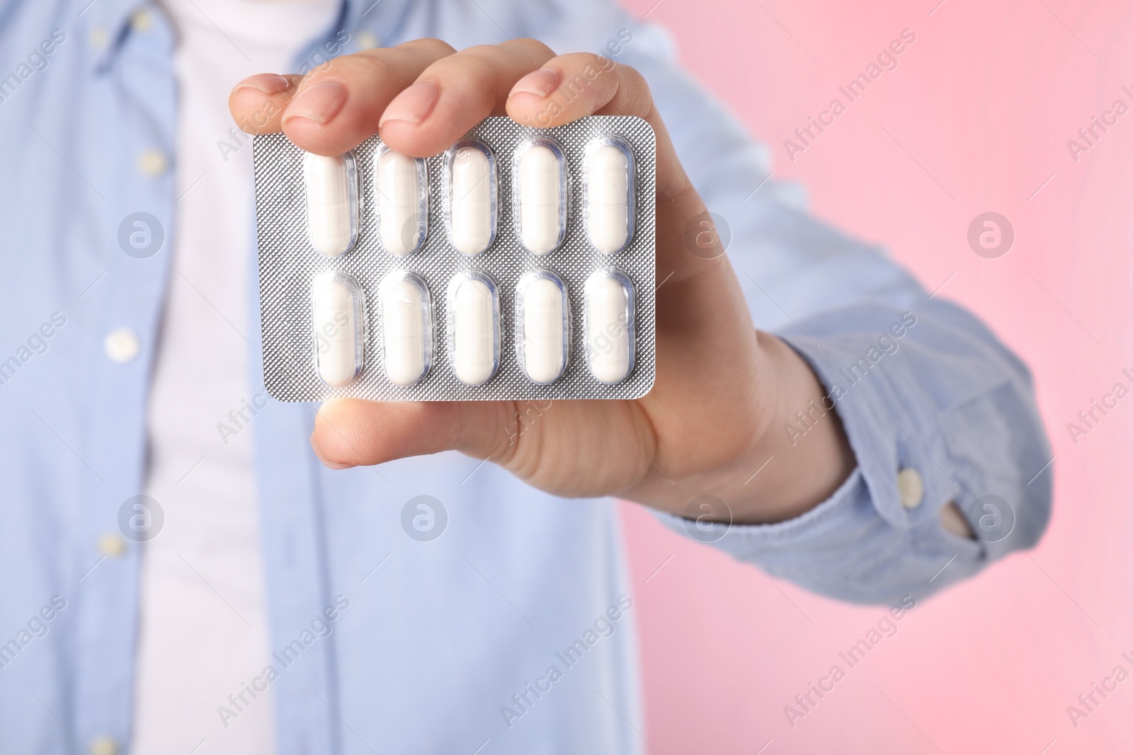 Photo of Woman holding blister with antibiotic pills on pink background, closeup